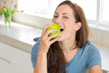 Smiling young woman eating apple in kitchen