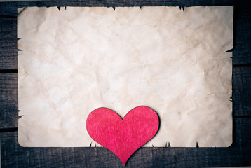 Old card on aged wood decorated with wooden heart 