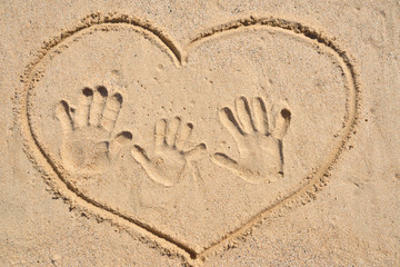 Happy family with kid hands print on sand with drawing heart.