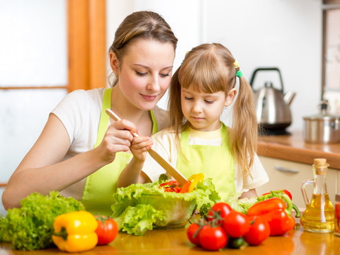 mother teaching kid daughter mixing salad at kitchen