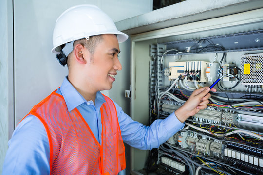 Asian Electrician at panel on construction site
