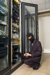 robber in black mask hack server room downloading data on laptop