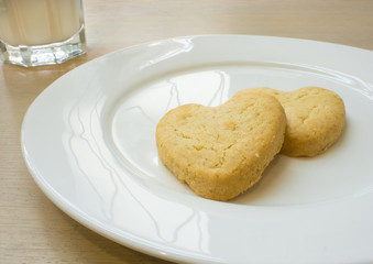 Heart cookies on white plate and glass of milk.