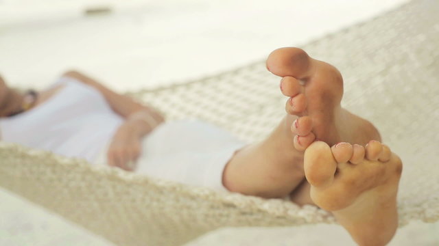 Woman lying on hammock on exotic beach, focus on her feet