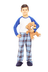 Full length portrait of a boy in pajamas holding teddy bear