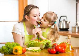 mother feeding kid vegetables in kitchen
