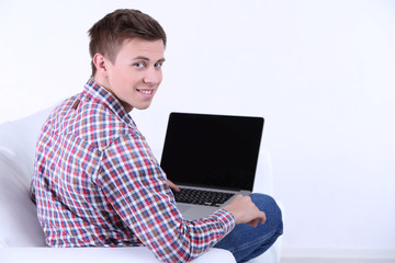 Guy sitting on sofa with laptop on white background