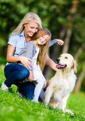 Mother and daughter with labrador retriever sitting on thegrass
