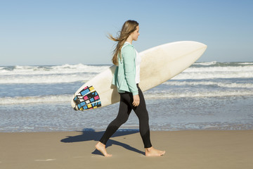 Tenage girl walking in the beach with her surfboard