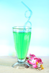 Glass of cocktail, on sand, on bright background