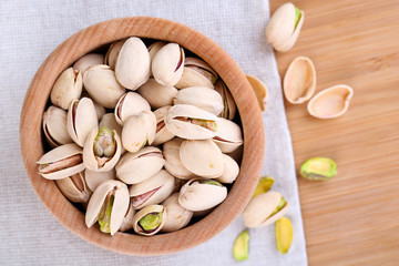 Pistachio nuts in wooden bowl on fabric background
