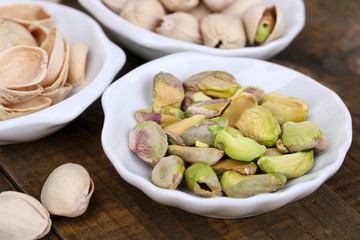 Pistachio nuts in small bowls on wooden background
