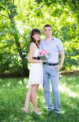 man and woman standing on the grass on a background of green tre