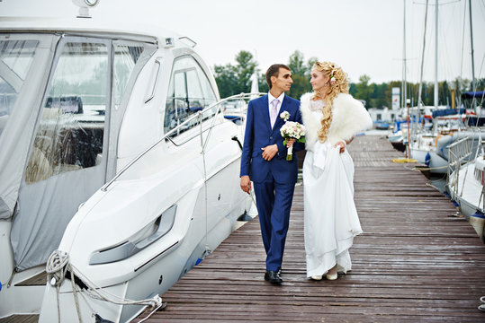 Romantic bride and groom go to the pier with yachts boats