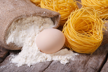 dry pasta in the form of nests, a raw egg and a bag of flour