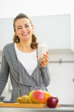 Happy young woman drinking smoothie in kitchen