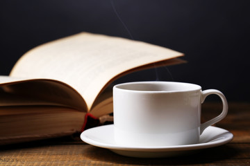 Cup of hot coffee with book on table on dark background