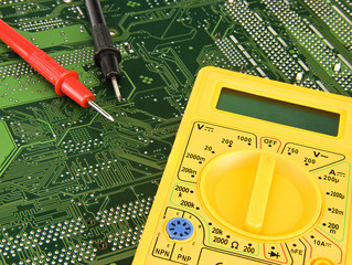 Yellow multimeter on green motherboard pcb