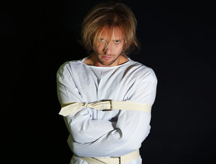 Mentally ill man in strait-jacket on black background