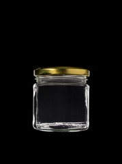 Transparent glass jar on black background, with the closed gold color top