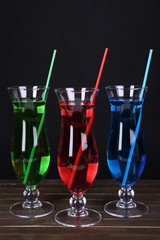 Glasses of cocktails on table on black background