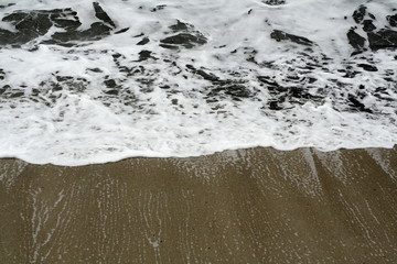 white sea waves crashing and receding on sandy beach