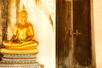 Golden meditating buddha next to close door at Wat Phutthaisawan