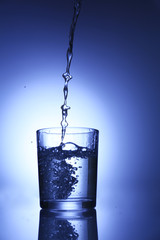 Pour water from  pitcher into  glass, on dark blue background