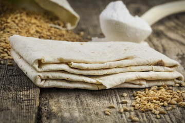 Pita bread with grains and flour on old wooden table