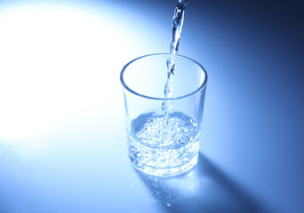 Pour water from  pitcher into  glass, on dark blue background