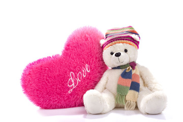 Toy teddy bear sitting with heart-shaped pillow