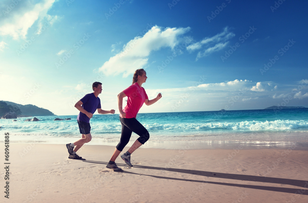 Wall mural man and women running on tropical beach at sunset