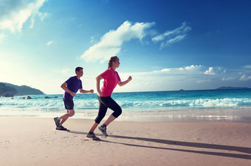 Man and women running on tropical beach at sunset