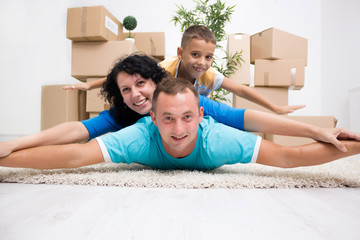 Happy couple with a kid in their new home laying on the floor wi