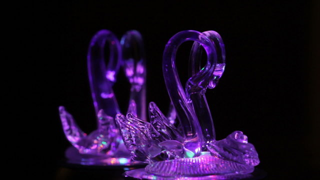 Couple of glass swans in the dark in front of the mirror
