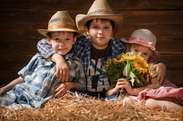 Three laughing children on hay in a hangar