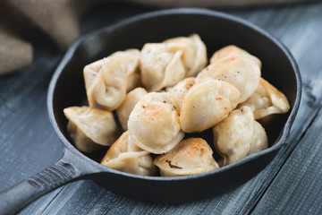 Roasted pelmeni in a pan on wooden surface, horizontal shot