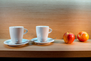 two teacups and two apples on wooden background