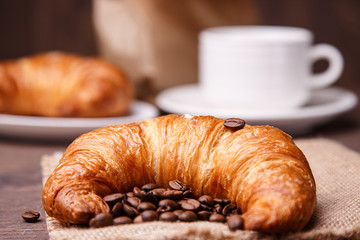 Croissant with coffee beans and a cup on the backround