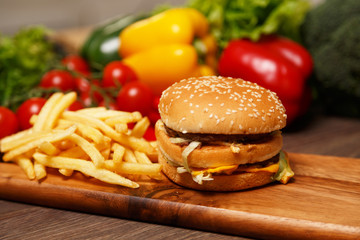 Tasty hamburger and crispy fries on a wooden board