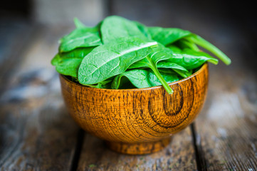 Fresh spinach in a bowl on rustic wooden background