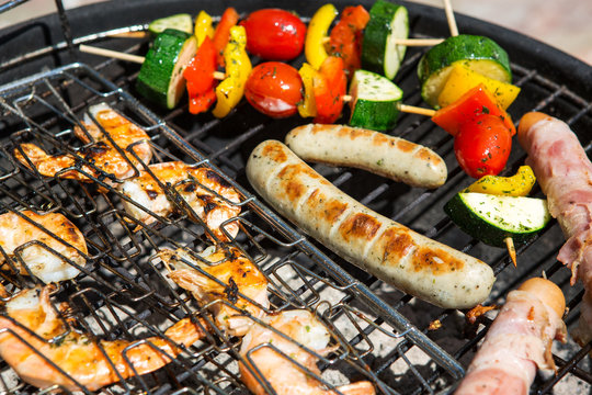 Sausages, big prawns and vegetable skewers smoking on grill
