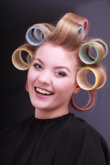 Happy blond girl hair curlers rollers by hairdresser in salon