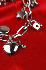Silver charm bracelet on red, love heart in foreground 