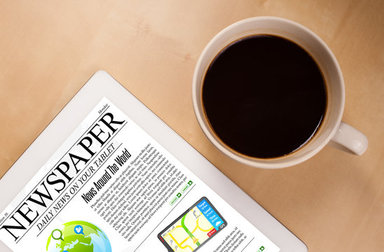 Tablet pc shows news on screen with a cup of coffee on a desk