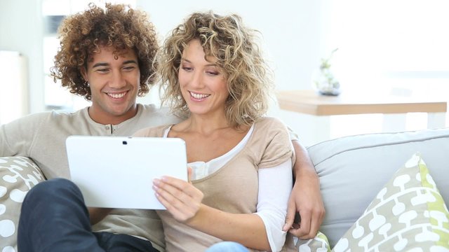 Cheerful couple having fun using tablet in sofa