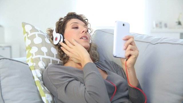 Smiling woman laying in couch and listening to music