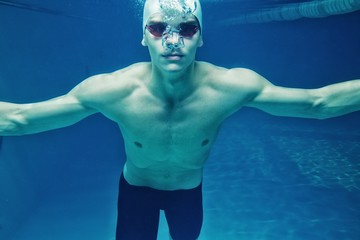 Man in swim cap and googles under water in swimming pool