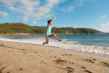 young boy playing running and jumping on the beach