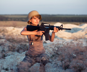 Young female soldier dressed in a camouflage with a gun in the o